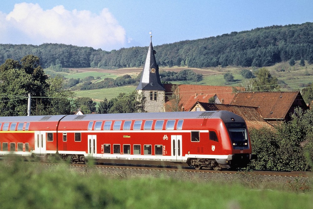 一张红火车在德国的乡村骑行的照片。