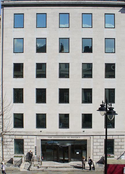 一栋不起眼的灰色建筑的立面，有27个窗户和一个宽阔的入口。