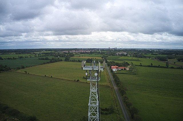 一张5G通信塔的航拍照片，周围环绕着开放的绿色田地。