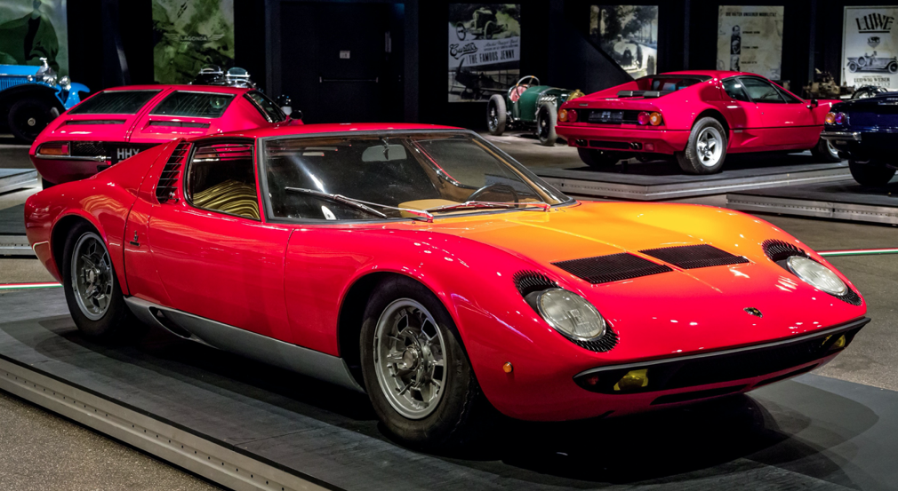 前面的红色兰博基尼米拉（Lamborghini Miura）的照片，背景其他跑车和超级跑车。