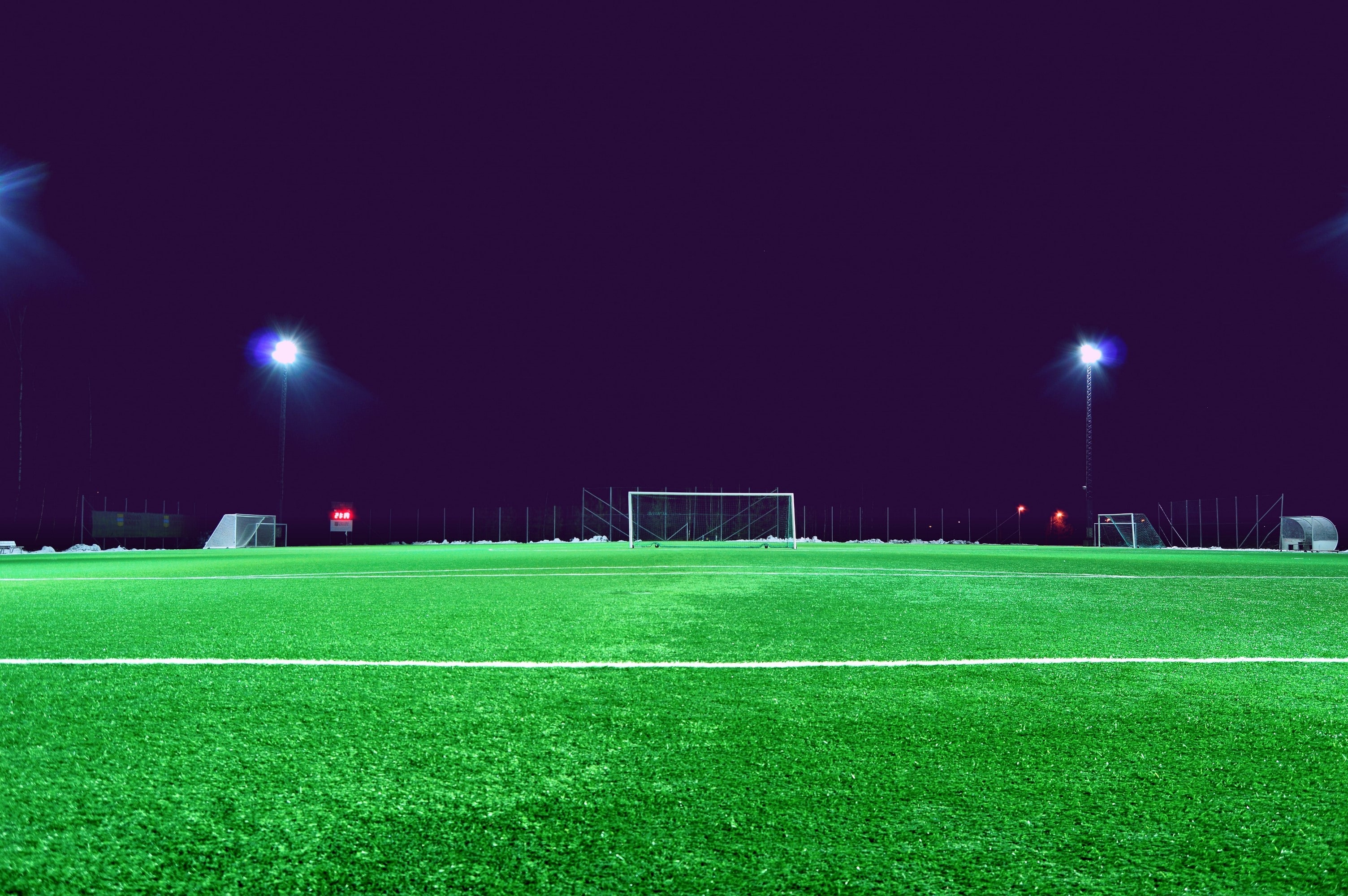 夜间的绿色足球场的照片，距离球门两侧的两侧有一个黑暗的天空和两个高的LED灯。